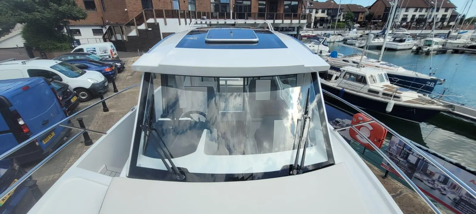 Aerial view of a boat's cockpit with a panoramic windshield, parked at a marina surrounded by various boats.